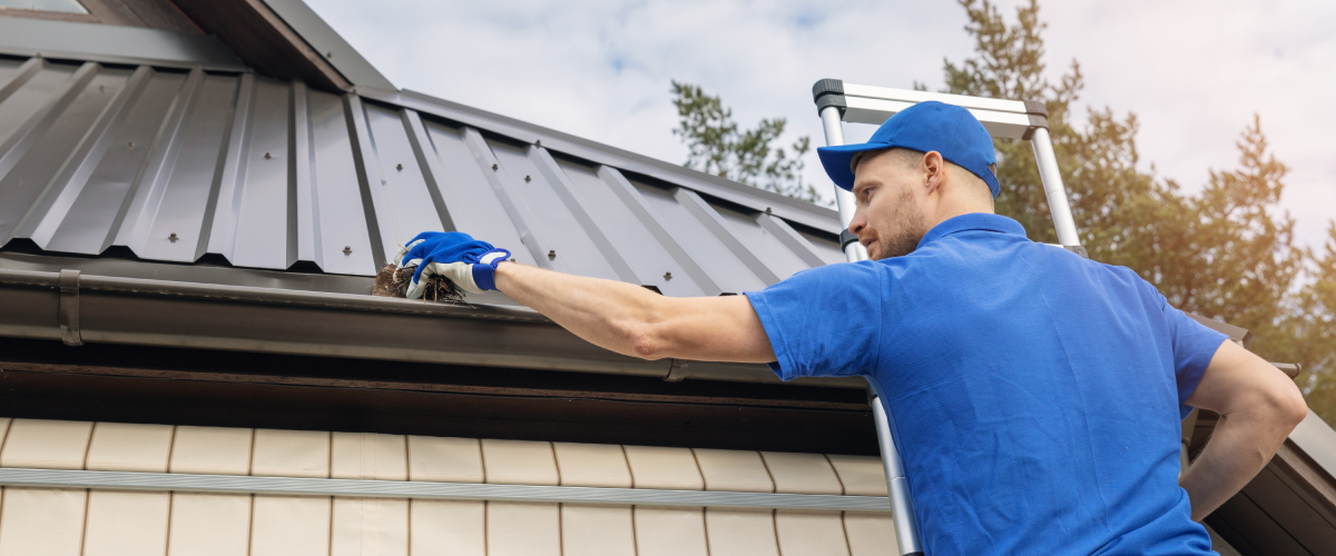 Man removing debris from a roof gutter.